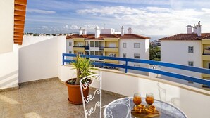 A balcony with a potted plant, a table with glasses and pastries, and a view of buildings with red roofs.