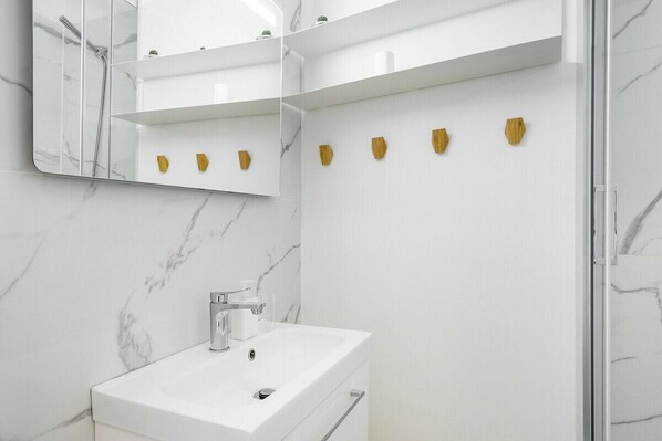 A modern bathroom with a white marble sink, a large mirror, and a shower.