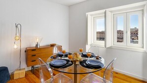A dining area with a round glass table set for four, a wooden sideboard, and a city view through large windows. - Lisbon's Horizon Retreat: A View to Remember (Lisboa)