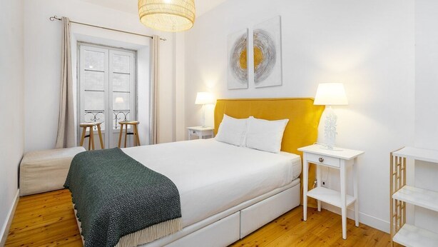 Une chambre à coucher avec un lit, des tables de chevet, une lampe suspendue et une fenêtre avec des rideaux.