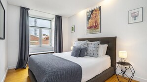 Un dormitorio con una cama grande, una ventana con cortinas, un cartel en la pared y una mesita de noche con una lámpara.