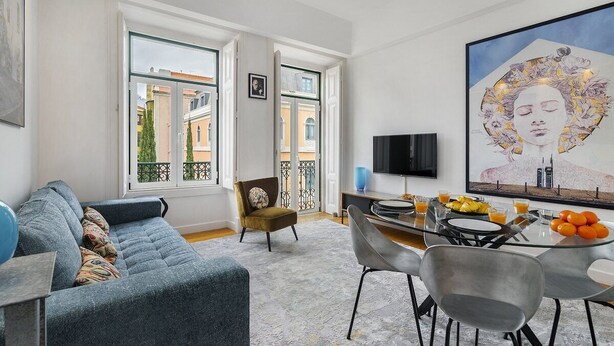 Una sala de estar moderna con un sofá, una mesa de comedor con sillas, un televisor y un cuadro grande en la pared.
