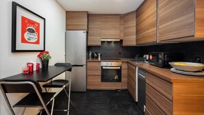 A modern kitchen with wooden cabinets, a stainless steel refrigerator, an oven, a microwave, and a dining area with a table and chairs.