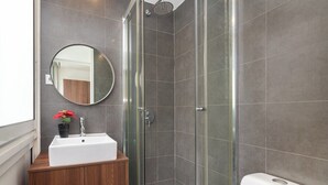 A modern bathroom with a glass shower enclosure, a white sink, and a wooden vanity.