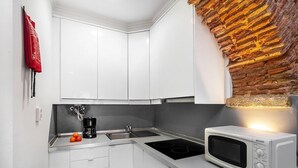 A modern kitchen with white cabinets, a built-in stove, a microwave, and a brick accent wall.