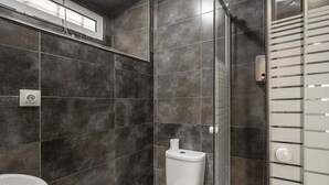 A modern bathroom with dark tiles, a white toilet, a sink, and a shower area.