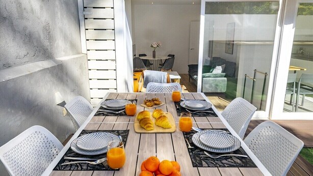 A dining area with a wooden table set for six, surrounded by white chairs with black patterns. There are plates, cutlery, and a centerpiece of oranges and croissants. - Suburban Serenity: Family Home with Pool (Algés)