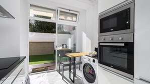 A compact kitchen with a washing machine, a microwave, and a dining area with a table and chairs. - Suburban Serenity: Family Home with Pool (Algés)