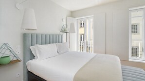 A modern bedroom with a bed, a bedside lamp, a window, and a view of the outside.