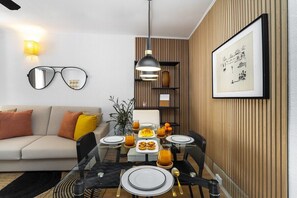 Un espace repas moderne avec une table en verre disposée pour quatre personnes, entourée de lambris en bois et agrémentée d’une œuvre d’art encadrée au mur.