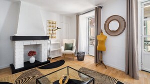A living room with a white brick fireplace, a yellow chair, a round mirror, and a black-framed glass coffee table. - Stylish Family Residence in the Heart of Chiado (Lisboa)