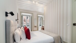 Ein modernes Schlafzimmer mit einem großen Bett, zwei Fenstern, einem Nachttisch und einer Wandlampe.