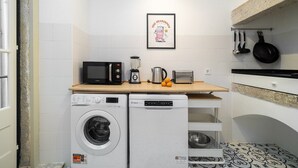 Une cuisine compacte équipée d’un lave-linge, d’un four à micro-ondes, d’un grille-pain et d’ustensiles suspendus.