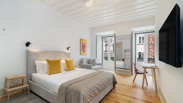 Une chambre à coucher avec un lit, une table de chevet et une chaise. Une porte donne accès à une autre pièce.