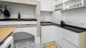 Une cuisine de taille réduite avec des meubles blancs, un plan de travail noir et un revêtement mural décoratif.