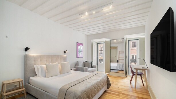 A modern bedroom with a large bed, a desk, and a chair. There is a door leading to a balcony. - Stylish Flat in Downtown Lisbon (Lisboa)