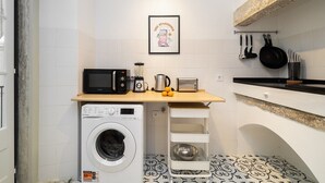 A compact kitchen with a washing machine, microwave, toaster, and hanging pots. - Stylish Flat in Downtown Lisbon (Lisboa)