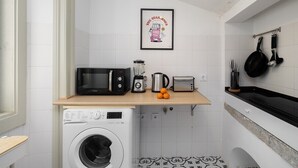 Eine kompakte Küche mit Waschmaschine, Mikrowelle, Toaster und Wasserkocher auf der Arbeitsfläche.