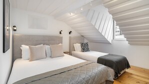Ein Schlafzimmer mit zwei Betten, einer geneigten Decke und einem Fenster mit Blick auf einen Balkon.