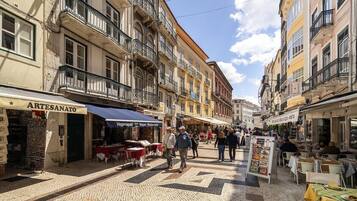 Rua com lojas e mesas ao ar livre, calçada de pedra e edifícios com varandas.