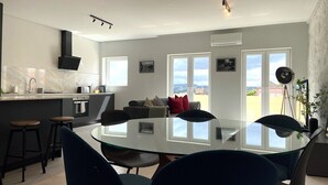 A modern kitchen with a central island, bar stools, and a dining area with a glass table and chairs.