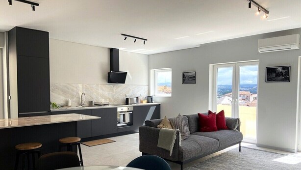 A modern kitchen with a central island, a dining area with a glass table, and a living space with a sofa and a view of the city.