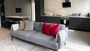 A modern living room with a grey sofa, red and black cushions, a small coffee table, and a TV mounted on the wall.