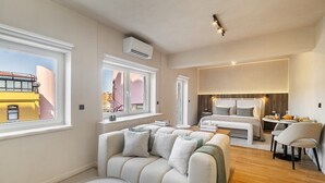 Ett modernt hotellrum med en soffa, ett matbord, en säng och stora fönster med utsikt över staden.