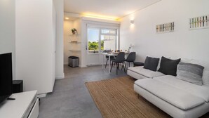 Ett modernt vardagsrum med en vit soffa, en tv och en matplats med ett bord och stolar.