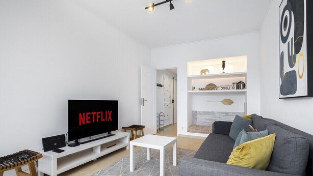 A modern living room with a flat-screen TV displaying 'NETFLIX', a grey sofa with cushions, a white coffee table, and a wooden bench. - Peaceful Algés Family Home away from City Noise (Algés)