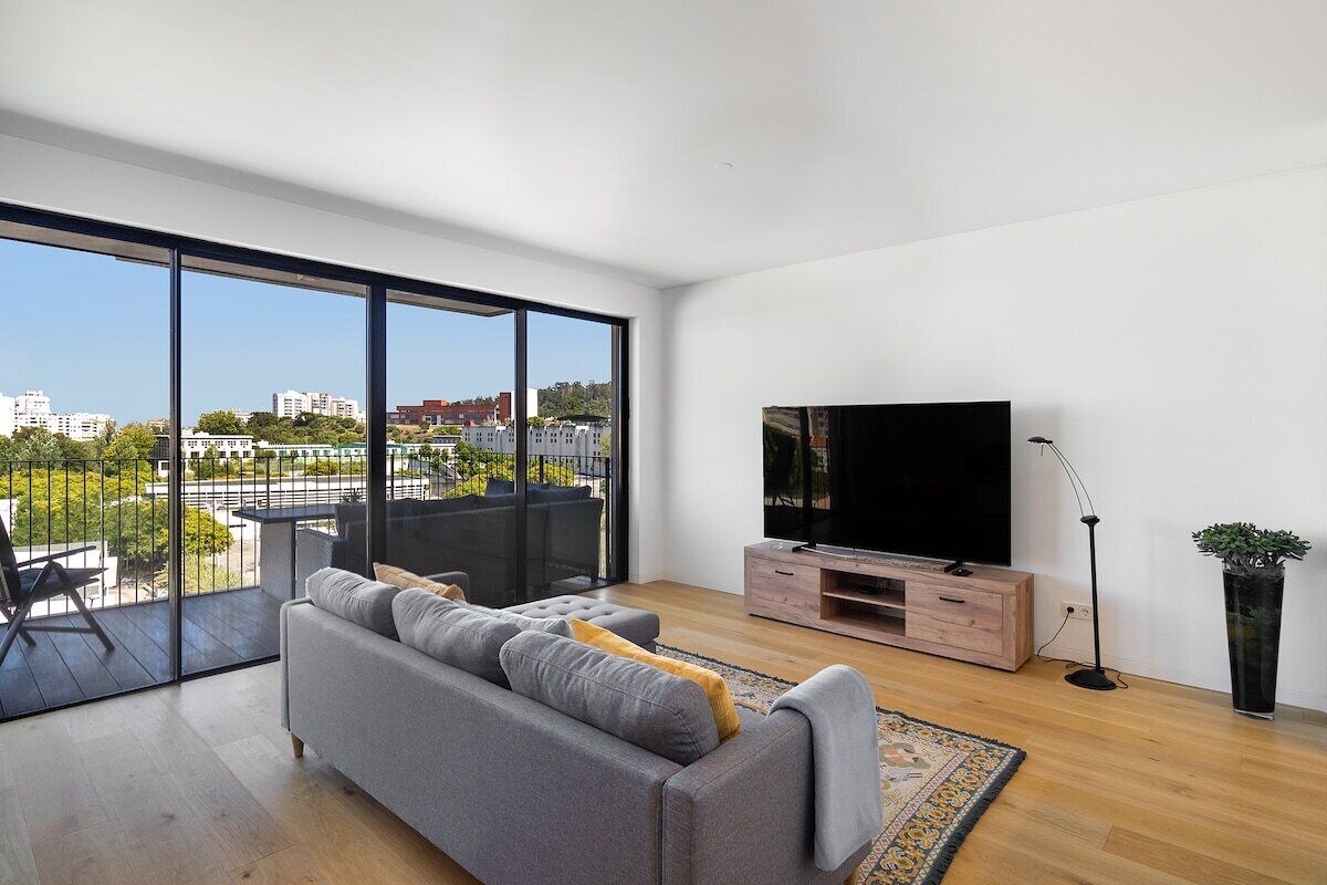 Ein modernes Wohnzimmer mit großem Fenster, einem grauen Sofa, einem Flachbildfernseher und einer Holz-Unterhaltungsanlage.