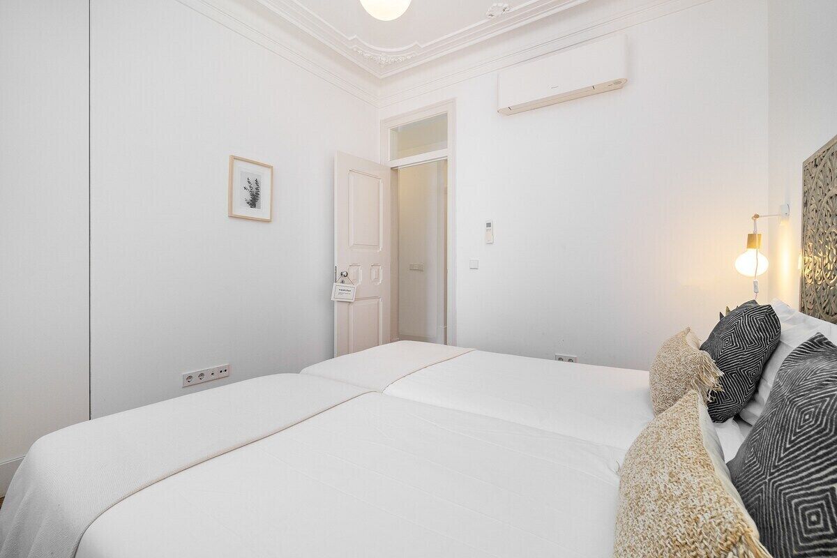 Une chambre d’hôtel avec un grand lit, une table de chevet, une lampe et une porte donnant sur une autre pièce.