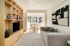 A modern living room with a sofa, TV, wooden shelving, and a dining area. - Modern & Elegant Apartment in Central Lisbon (Lisboa)