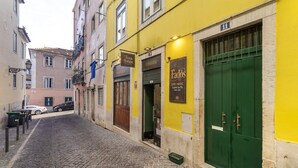 A narrow cobblestone street lined with buildings, including a yellow building with a green door and signs for 'Fados Live Music' and 'Vinho da Rua'.