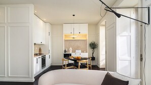 A modern kitchen with white cabinetry, a dining area with a round table, and a sofa with a brown pillow.