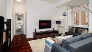 A modern living room with a flat-screen TV, a sofa, a coffee table, and a bookshelf.