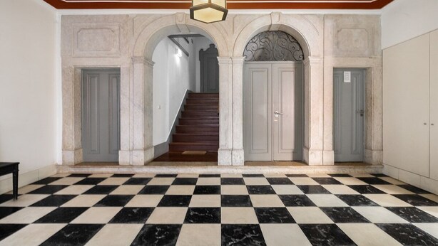 A hallway with a checkered floor, a staircase, and a light fixture above.