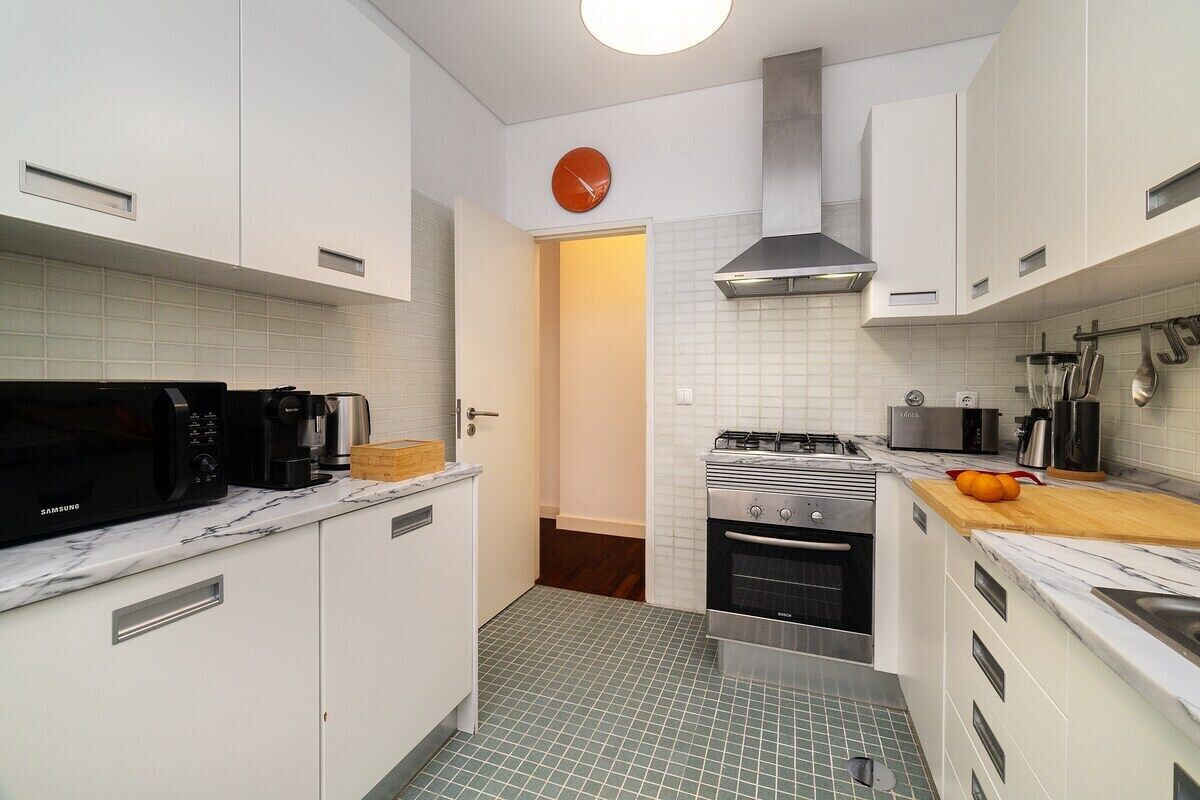 Une cuisine moderne avec des meubles blancs, un four à micro-ondes, une cuisinière et une horloge au mur.