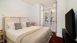 A hotel room with a bed, bedside table, TV, and a door leading to a balcony.