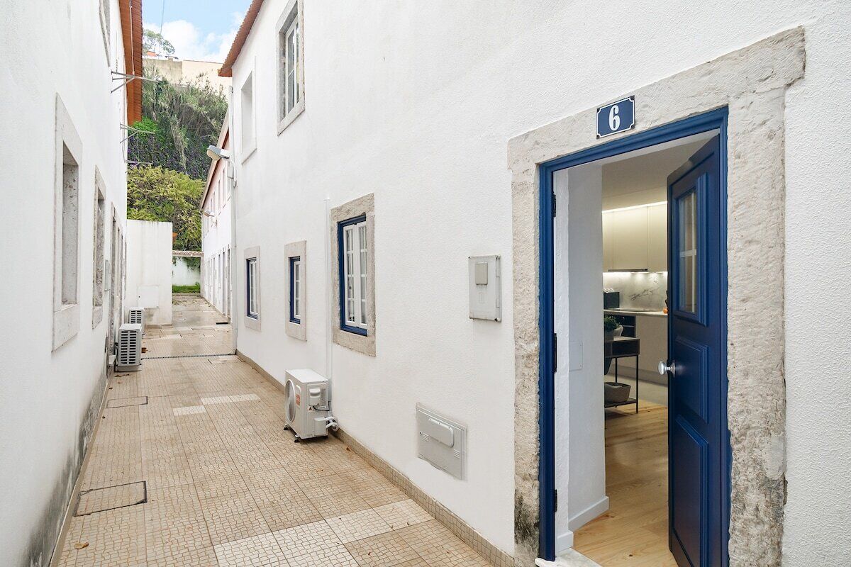 A narrow corridor with a tiled floor, white walls, and a blue door marked with the number 6.