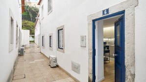 Un corridoio stretto con pavimento piastrellato, pareti bianche e una porta blu con il numero 6.