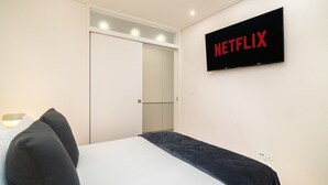Una camera da letto con un letto, un armadio e una TV a muro che mostra il logo di Netflix.