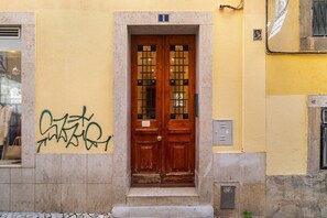 Eine Holztür mit doppeltem Flügel und einer kleinen Stufe davor, eingebaut in ein Gebäude mit gelber Wand und einem Fenster zur Linken.