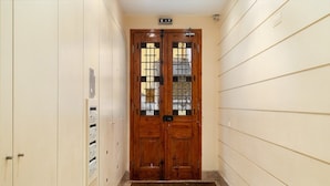 Un couloir avec une porte double en bois, une fente pour le courrier et un sol carrelé.