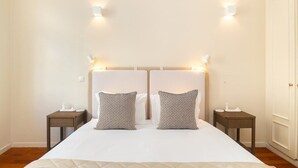 Un lit double avec une couette blanche, deux coussins à motifs et deux tables de chevet avec des lampes.