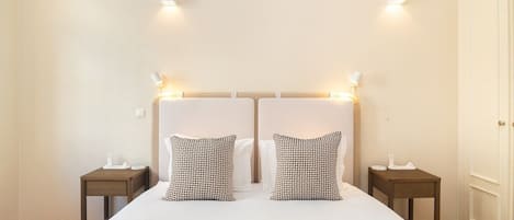 A double bed with a white duvet, two patterned pillows, and two bedside tables with lamps.