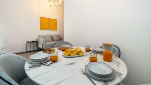 A dining area with a round marble table set for breakfast, including plates, glasses, and a pitcher of orange juice.