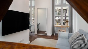 A modern living room with a flat-screen TV, a sofa, a dining area with a table and chairs, and large windows.