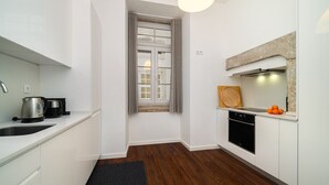A modern kitchen with white cabinets, a black countertop, a built-in oven, and a window with grey curtains.