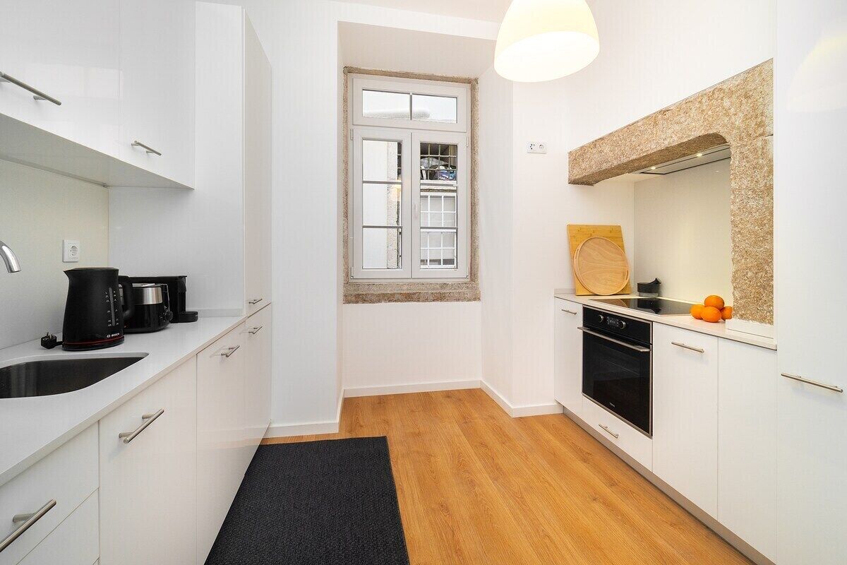 A compact kitchen with white cabinets, a black countertop, a built-in oven, and a window with a view.